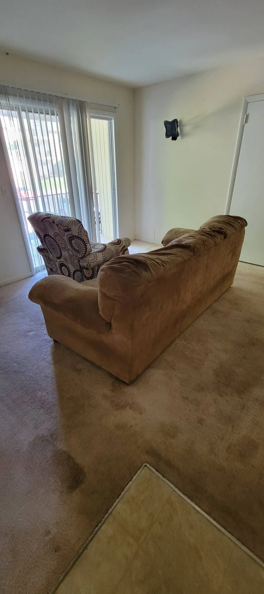 Old brown couch and patterned armchair in an apartment living room before removal